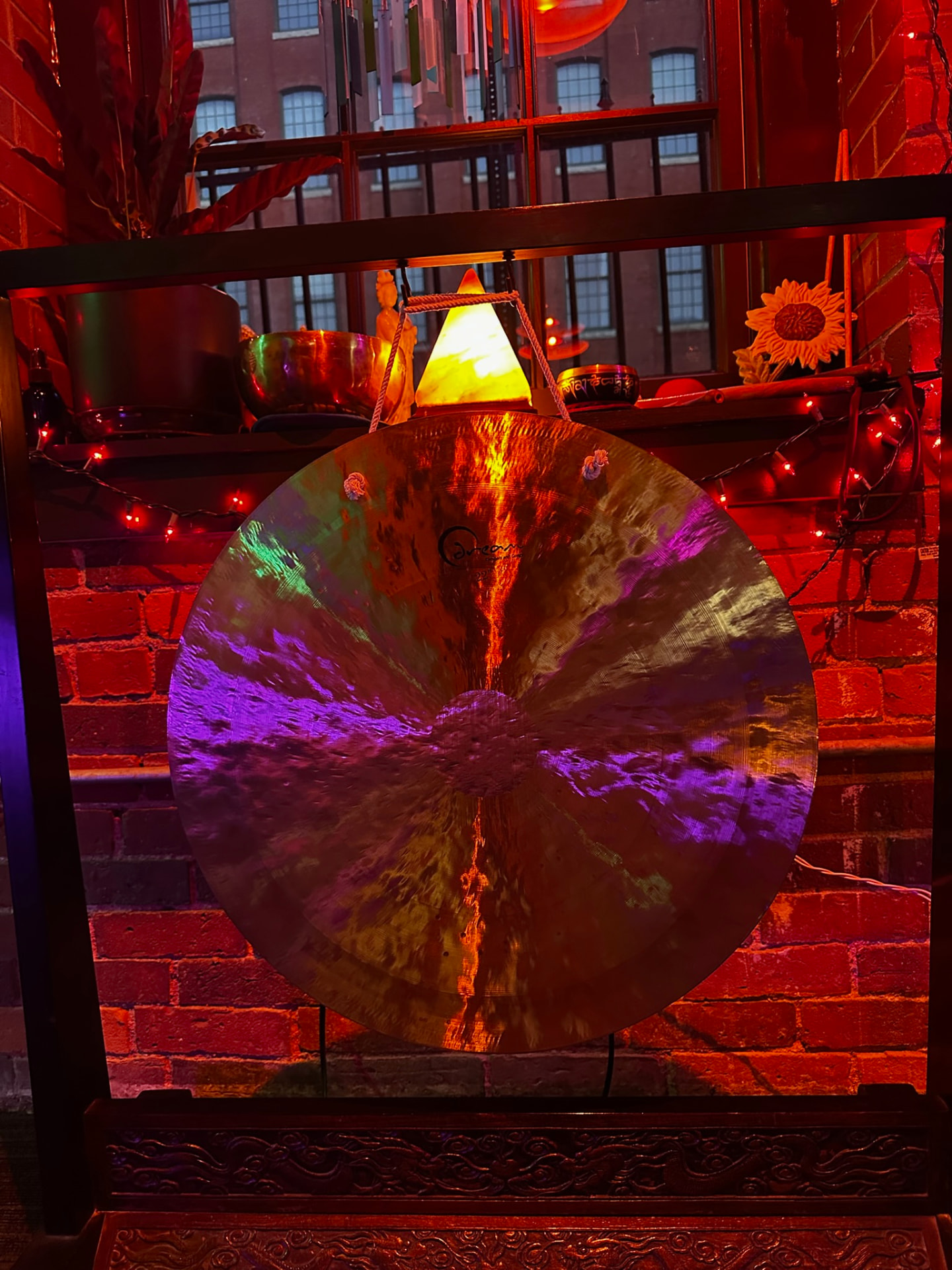 A large hammered gong lit in purple and orange against a brick wall